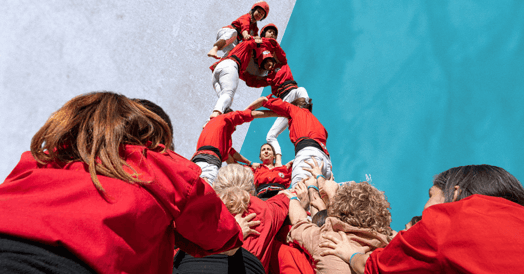 Several people in red jackets and white pants lifting each other into a human tower.
