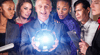 A group of six people gathered around a man in a suit holding a glowing crystal ball.