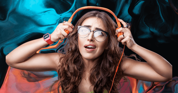 A woman with a perplexed expression removing a pair of orange headphones.