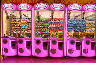 Italian Arcade: A row of pink and white claw machines in Italy filled with licensed plushies like Mickey Mouse and Mario.