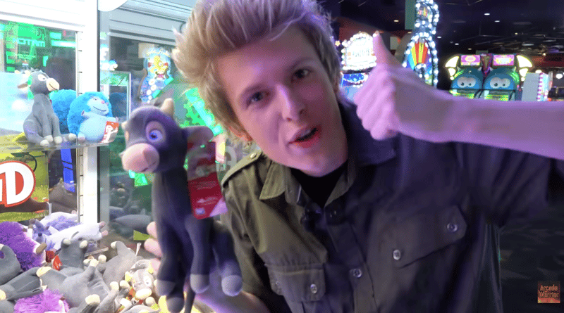 Arcade Warrior: YouTuber Erik Kane gives a thumbs-up while holding a plush donkey prize in an arcade.