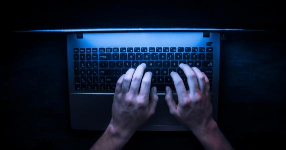 A pair of hands on a keyboard in a darkened room.