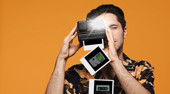 Polaroid Photographer: A man in a patterned shirt holds a vintage black Polaroid camera up to his eye against a solid orange background.
