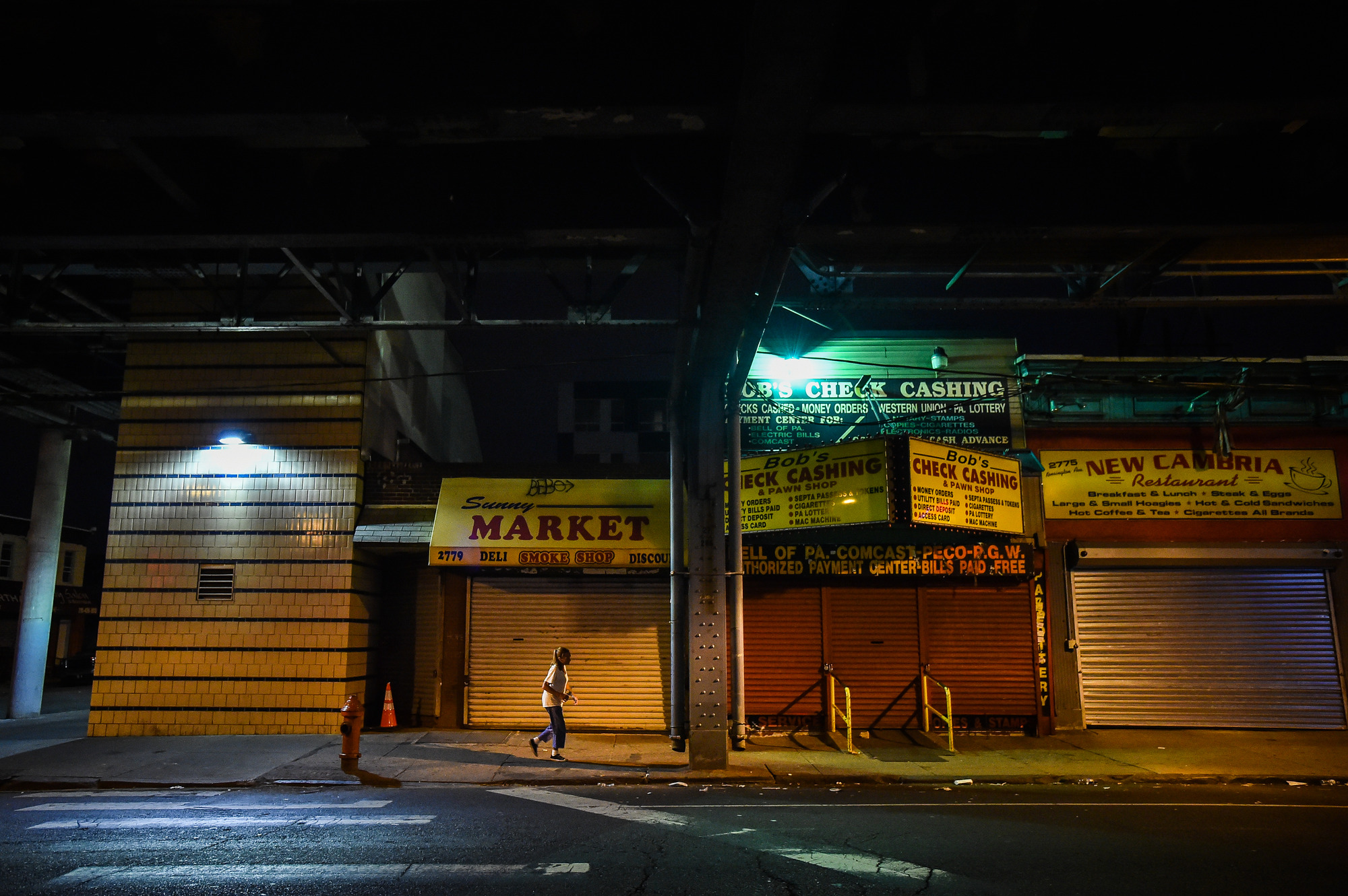 Kensington Avenue at night with check cashing shops and shuttered storefronts lit by fluorescent signs.