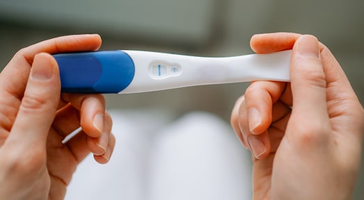 Two hands holding a modern stick pregnancy test with a visible result window.
