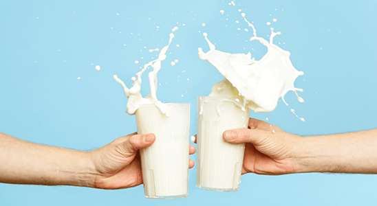 Two glasses of milk being clinked, splashing milk.