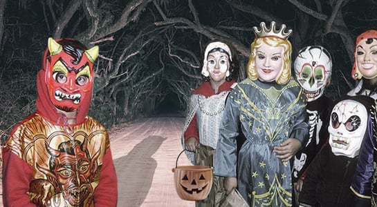 A group of children in various, slightly sinister vintage Halloween costumes, including a red devil, a queen, and several skeletons/ghouls, stand on a dark, tree-lined road.