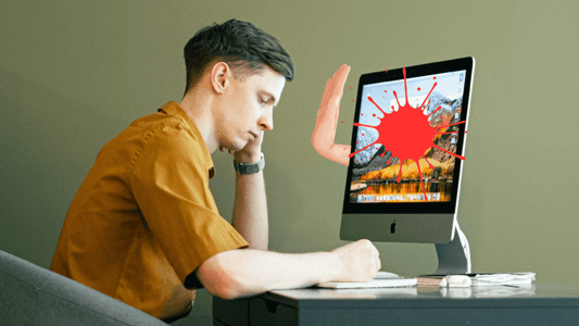 A white brunette man sits in front of a computer. There is a large red splat on the monitor and a white hand coming from the monitor making a stop signal.  