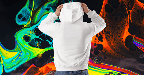 A man wearing jeans and a white hoodie with the hood pulled up stands facing away from the camera. 