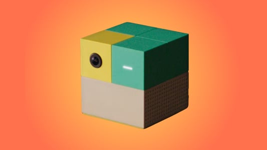 A Nex, a square gaming console with a beige bottom and yellow and teal top.