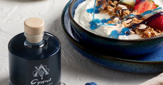 A yogurt parfait drizzles with blue honey next to a bottle of blue honey.