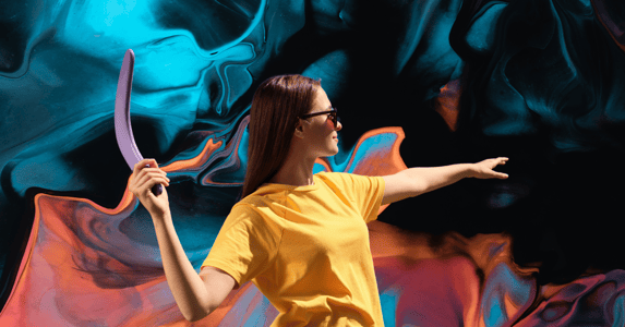 A woman in a yellow T-shirt and sunglasses preparing to throw a boomerang.