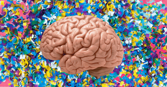 A brain in front of a colorful background made up of small plastic pieces.