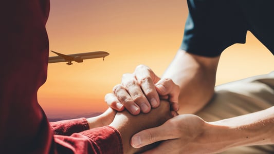 Two people hold hands while a plane flies in the background.