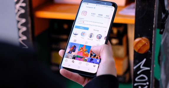 A hand holding a phone, its screen open to Instagram.