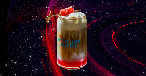 A raspberry danish latte from Little Joy Coffee in a branded glass.