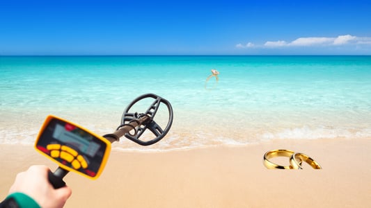 A metal detector hovering over a golden ring on the beach.
