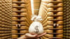A hand holds a sack of money in front of a large collection of parmesan cheese wheels
