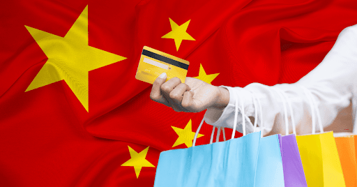 A hand holding shopping bags and extending a credit card in front of China’s flag. 