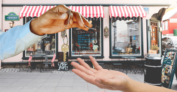 An outstretched hand offers a key to another outstretched hand in front of a cafe. 