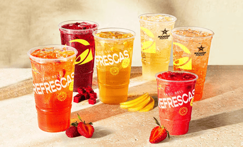 Several plastic cups filled with ice and red, orange, and yellow sodas. The cups read, 'Taco Bell Refrescas.'