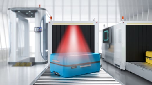 A blue suitcase going through a TSA baggage carousel with a red light shining on it. 